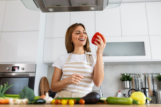 Photo Of Young Woman Smiling With Red Bell Pepper While Cooking And Making Salad With Fresh Vegetables In Kitchen Interior At Home