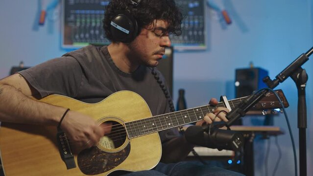 professional musician recoding new album playing acoustic guitar in recording studio