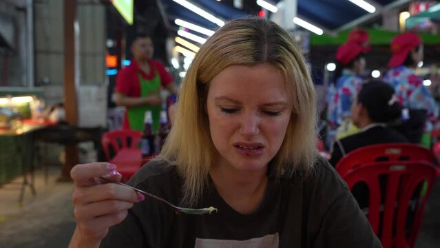 A young blonde woman makes faces while eating something that tastes bad.