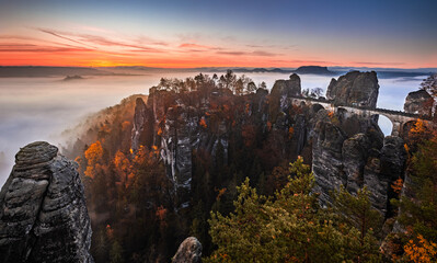 Saxon, Germany - Panoramic view of the Bastei bridge on a sunny autumn sunrise with colorful foliage and heavy fog under the valley. Famous for the rock formation in Saxon Switzerland National Park
