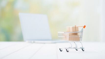 Mini Tiny cart with boxes beside laptop with blur background. Concept banner online shopping E-commerce.
