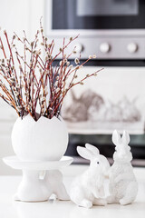 A bouquet of willow twigs for the Orthodox Palm Sunday holiday. Willow in a white egg and Easter bunnies in the interior of a modern white kitchen. - obrazy, fototapety, plakaty