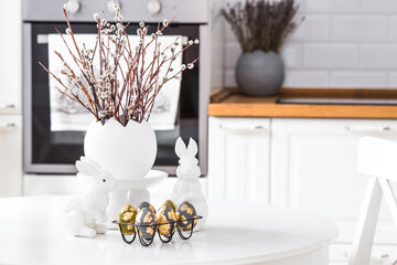 A bouquet of willow twigs for the Orthodox Palm Sunday holiday. Willow in a white egg, Easter bunnies and Easter eggs in the interior of a modern white kitchen.