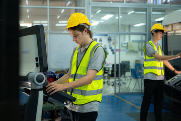 Young man factory worker wearing a hard hat looking at a computer screen used to control production.