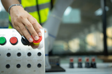 Close-up of hand pressing the stop button on the control panel of an industrial machine.