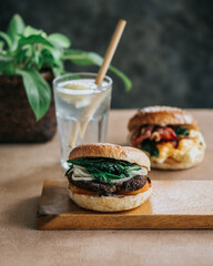 A close-up of a sandwich on a cutting board with bread, lettuce, tomato, cheese, and glass drink on wooden plate