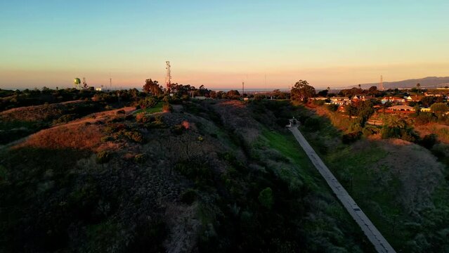 Aerial drone forward moving shot over town houses along hills fields during evening time.