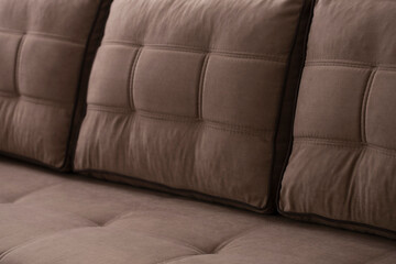 Close-up of stitched quilted plump soft pillows on a beige-brown sofa. Upholstered furniture made of combined velor fabric with a blurred background.