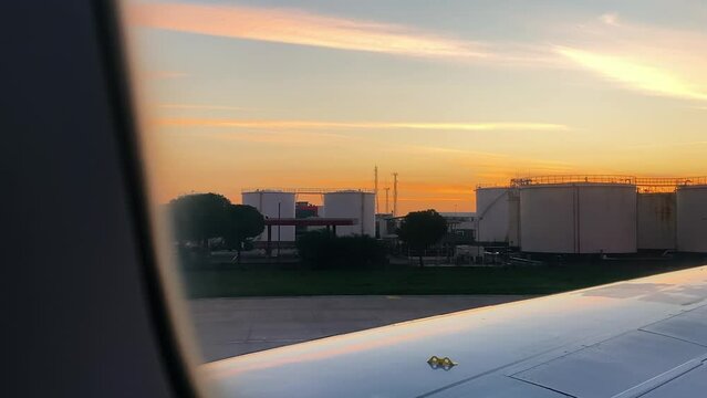 View from window of plane on fuel storage silos. Airplane on runway at sunset