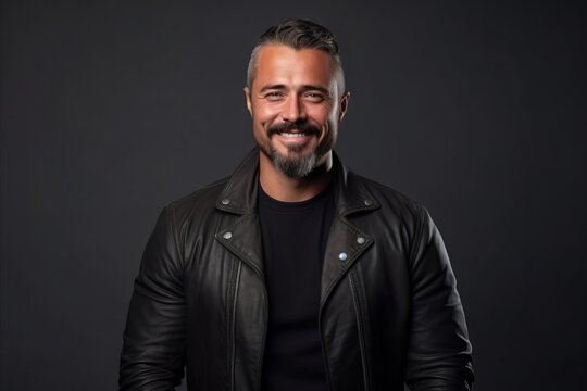 Handsome bearded man in a black leather jacket on a dark background.
