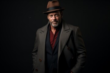 Handsome middle aged man in a hat and coat on a dark background