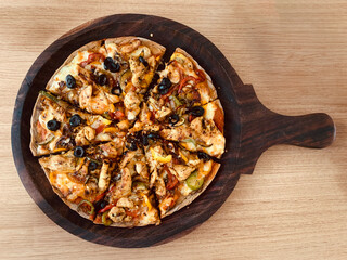 Pizza on a dark brown serving board on wooden table