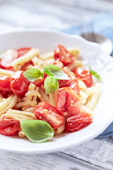 Casarecce pasta withe cherry tomatoes and fresh basil. Bright wooden background. Close up.	