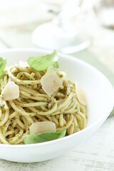 Spaghetti with olive pesto sauce and fresh basil. Bright wooden background. Close up	