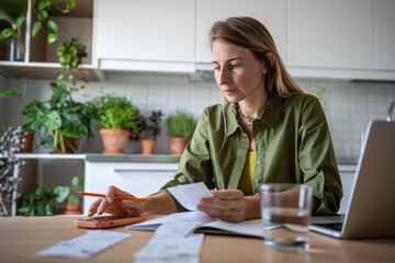 Financial literacy. Focused woman using smartphone calculating expenses, trying to analyze domestic budget, thinking how to pay debt, sitting at kitchen table. Savings, smart spending and consumption.