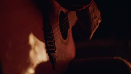 A man is playing guitar by the campfire. Relaxing during a hike in the evening