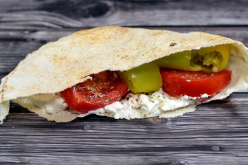Traditional Shami flat bread made of wheat and flour stuffed with white creamy cheese, slices of tomatoes, pieces of green chili peppers and thyme herb, a cheese sandwich in shami bread with vegetable