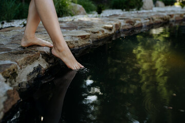 Unrecognizable young woman is dipping her foot in cool water of pond, refreshing and hardening concept.