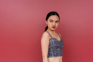 Portrait of a young Asian woman glancing back with a look of disdain, set against a bold red background, capturing an emotion of contempt.