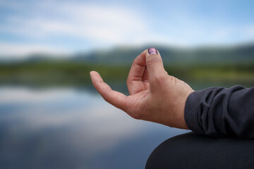 Yoga hand of a woman meditating in the lotus position in front of the water. 