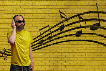 Man listening music with headphones in front of a yellow brick wall with graffiti music notes.