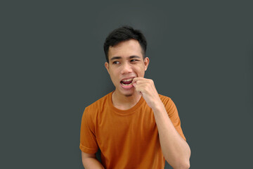 Something stuck in the teeth of a young Asian man, pulling with a hand on a plain background.