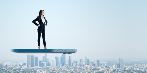 A futuristic concept of a confident businesswoman standing atop a giant smartphone, overlooking a...