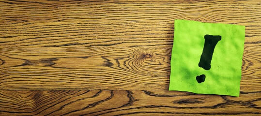 Close up of green note paper with exclamation mark on wide wooden desktop with mock up place. Questions and answers concept. 3D Rendering.