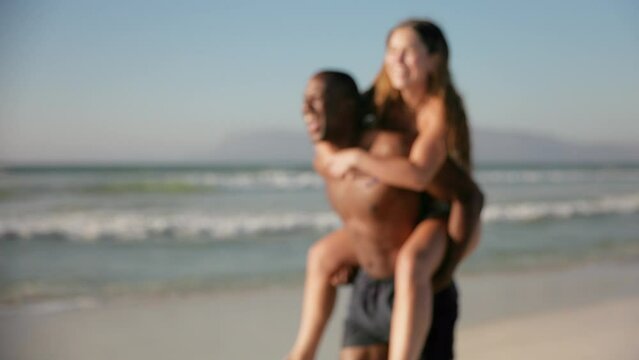 Camera tracks up shot of loving young couple in swimwear with man giving woman piggyback running along beach in South Africa - shot in slow motion