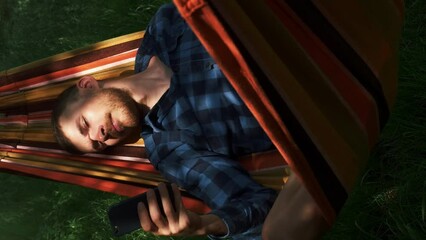 Man lying in hammock, relaxing and using smartphone. Vertical video