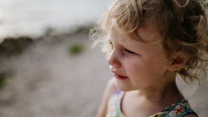 Portrait of crying blonde girl in summer outfit on walk during summer vacation, concept of beach holiday.