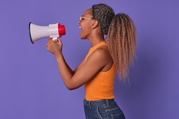 Young eccentric African American woman stands sideways with megaphone in hands urging everyone to...