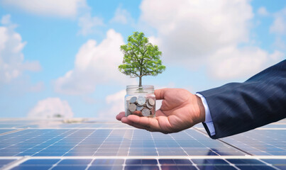 Close-up of a businessman's hand with A small tree grows out of money in a glass jar and coins on solar panels.Generative AI - Powered by Adobe