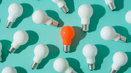 An orange lightbulb glowing among a group of white lightbulbs on a teal background, representing a unique idea or solution.