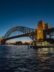Obraz premium Sydney by night and at sunset is a beautiful sight to behold. The city skyline, complete with the iconic Harbour Bridge, is a picture-perfect view of Australia.