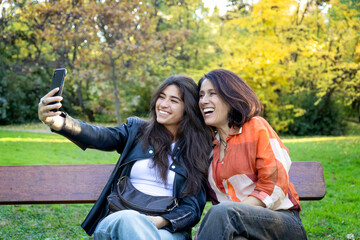 single mother with her teenage daughter sitting on a bench taking a photo with their phone