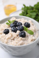 Delicious barley porridge with blueberries and mint in bowl on white table, closeup