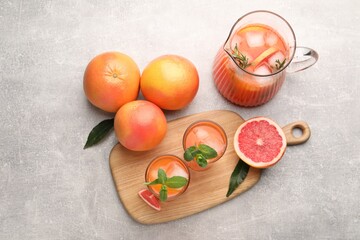 Tasty freshly made grapefruit juice, fruits and mint on light grey table, flat lay