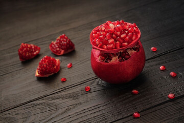 A ripe, red pomegranate is beautifully cut, posing on a wooden black table. Healthy, wholesome,...