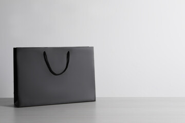 Black paper bag on white wooden table, space for text