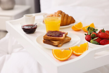 Tray with delicious breakfast on bed, closeup