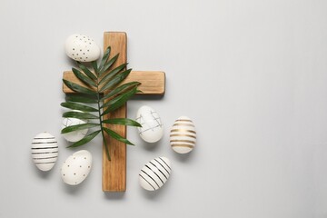 Wooden cross, painted Easter eggs and palm leaf on light grey background, flat lay. Space for text