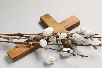 Wooden cross, painted Easter eggs and willow branches on light grey background