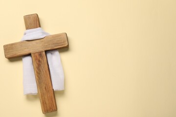Wooden cross and white cloth on beige background, top view with space for text. Easter attributes
