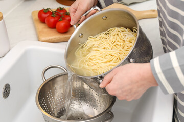 Woman draining pasta into colander at sink, closeup