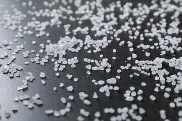 Scattered white natural salt on black table, closeup