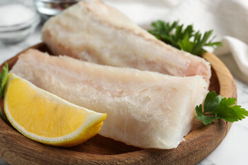 Fresh raw cod fillets with parsley and lemon on white table, closeup