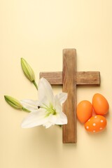 Wooden cross, painted Easter eggs and lily flowers on pale yellow background, flat lay