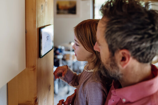 Girl helping father to adjust, lower heating temperature on thermostat. Concept of sustainable, efficient, smart technology in home heating and thermostats.