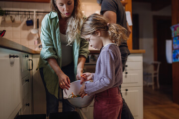 Girl helping parents put kitchen waste, peel and leftover vegetables scraps into kitchen...